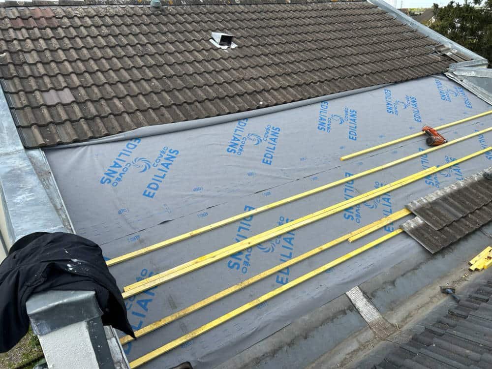 Pose de tuiles neuves sur liteaux lors d'une rénovation de toiture dans le Loiret
